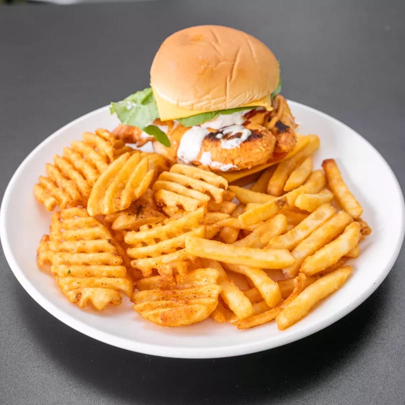 Chicken sandwich with cheese, lettuce, and sauce, served with waffle and regular fries on a white plate.