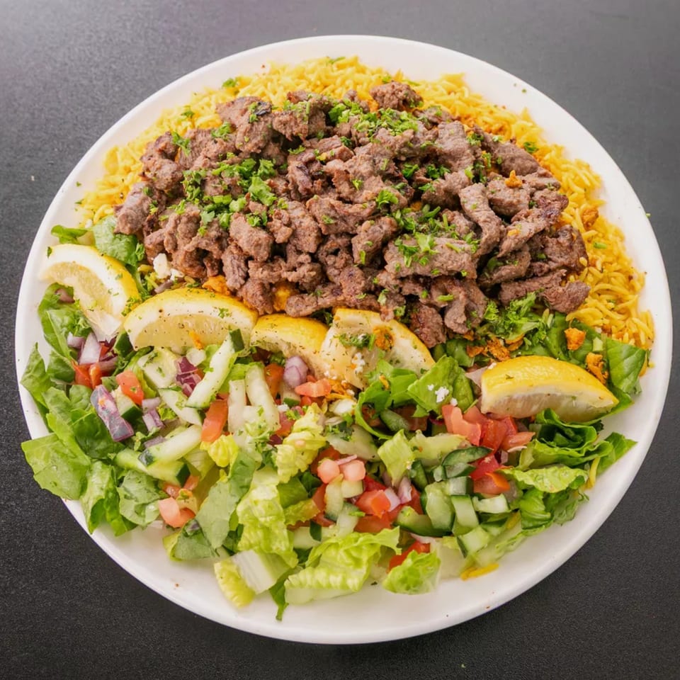 A white plate with yellow rice, seasoned beef, fresh green salad, and lemon wedges.