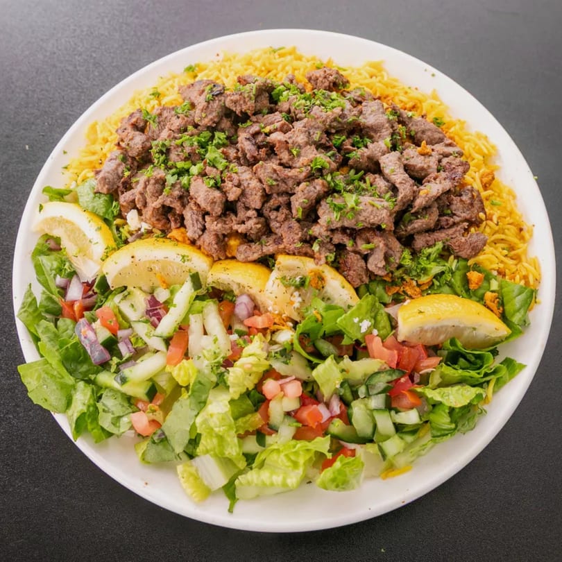 A white plate with yellow rice, seasoned beef, fresh green salad, and lemon wedges.