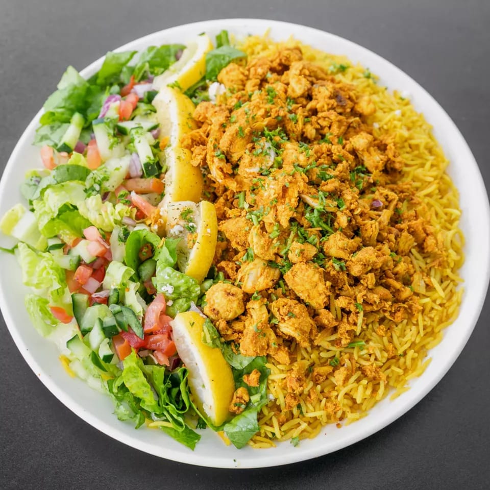 A white plate with yellow rice and chicken, a fresh salad, and lemon wedges.