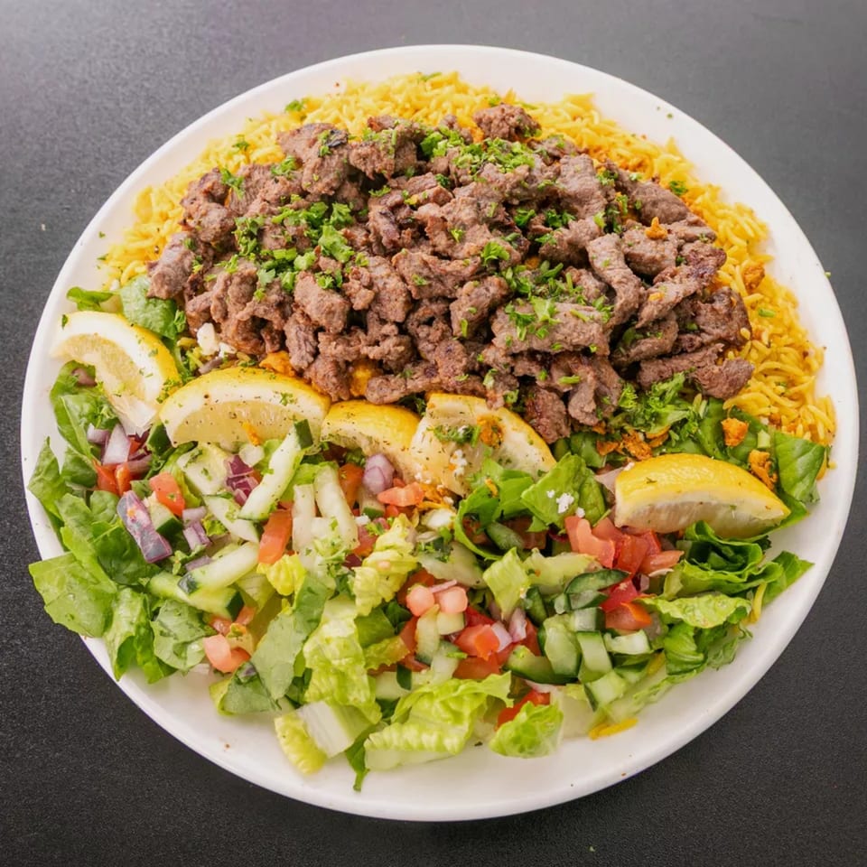 A white plate with yellow rice, chopped meat, and a fresh green salad with lemon wedges.